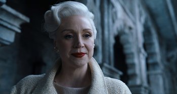 Movie still from “Wednesday” (2022), created by Miles Millar – An older woman with white hair wearing a white coat; Close Up shot, Over the shoulder angle
