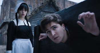 Movie still from “Wednesday” (2022), created by Miles Millar – A woman and a young man in a costume; Medium shot, Low angle