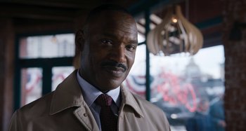 Movie still from “Wednesday” (2022), created by Miles Millar – A person wearing a suit and tie; Close Up shot, Over the shoulder angle