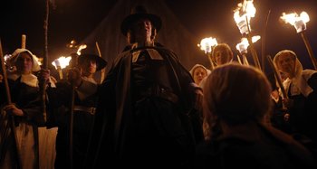 Movie still from “Wednesday” (2022), created by Miles Millar – A group of people standing next to each other in front of lit torches; Medium shot, Low angle