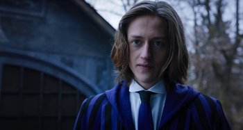 Movie still from “Wednesday” (2022), created by Miles Millar – A man with long hair wearing a suit and tie; Close Up shot, Low angle