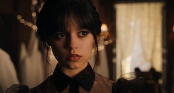 Movie still from “Wednesday” (2022), created by Miles Millar – A young woman wearing a black bow tie and a black shirt; Close Up shot, Over the shoulder angle