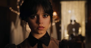 Movie still from “Wednesday” (2022), created by Miles Millar – A young girl wearing a black bow tie; Close Up shot, Over the shoulder angle