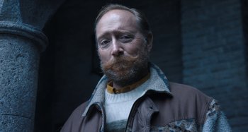 Movie still from “Wednesday” (2022), created by Miles Millar – A man with a beard and a jacket on; Close Up shot, Low angle
