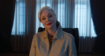 Movie still from “Wednesday” (2022), created by Miles Millar – A woman sitting in a chair wearing a jacket; Medium shot, Low angle