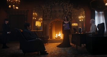 Movie still from “Wednesday” (2022), created by Miles Millar – A man and a woman dressed in black in front of a fireplace; Wide shot, Over the shoulder angle