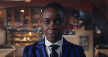 Movie still from “Wednesday” (2022), created by Miles Millar – A person wearing a suit and tie in front of a counter; Close Up shot, Low angle