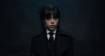 Movie still from “Wednesday” (2022), created by Miles Millar – A girl in a black coat and a black tie; Close Up shot, Overhead angle