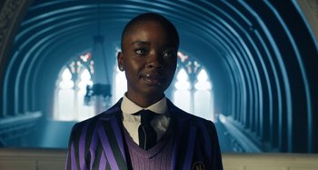 Movie still from “Wednesday” (2022), created by Miles Millar – A person in a purple and black striped jacket; Close Up shot, Low angle