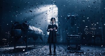 Movie still from “Wednesday” (2022), created by Miles Millar – A young girl standing in a dark room surrounded by confetti; Wide shot, Low angle