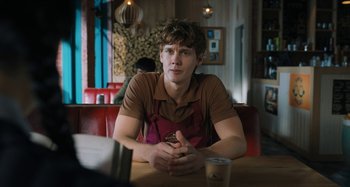 Movie still from “Wednesday” (2022), created by Miles Millar – A man sitting at a table in a restaurant; Medium shot, Over the shoulder angle