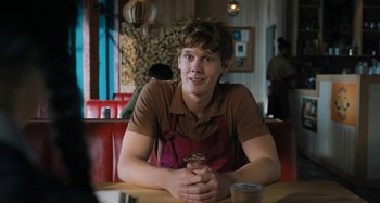 Movie still from “Wednesday” (2022), created by Miles Millar – A man sitting at a table in front of a cup of coffee; Medium shot, Over the shoulder angle