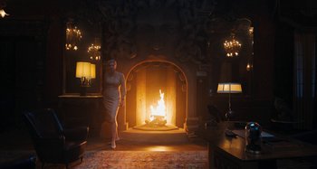 Movie still from “Wednesday” (2022), created by Miles Millar – A woman standing in front of an open fire place; Wide shot, Over the shoulder angle