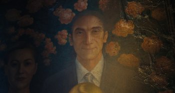 Movie still from “Wednesday” (2022), created by Miles Millar – A man in a suit and tie with flowers in the background; Close Up shot, Overhead angle