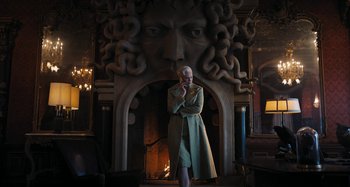 Movie still from “Wednesday” (2022), created by Miles Millar – A woman standing in front of a fire place; Medium shot, Low angle