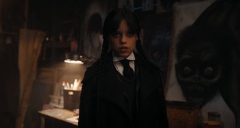 Movie still from “Wednesday” (2022), created by Miles Millar – A woman in a black coat and a tie; Medium shot, Low angle