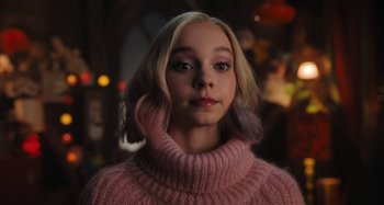 Movie still from “Wednesday” (2022), created by Miles Millar – A young blonde girl wearing a pink sweater; Close Up shot, Over the shoulder angle
