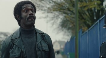 Movie still from “Small Axe” (2020), directed by Steve McQueen – A man standing on the side of the road looking up; Close Up shot, Over the shoulder angle