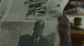 Movie still from “Small Axe” (2020), directed by Steve McQueen – A person holding a newspaper with a picture of a man in a hat; Extreme Close Up shot, High angle