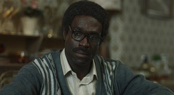 Movie still from “Small Axe” (2020), directed by Steve McQueen – A person wearing glasses and a sweater; Close Up shot, Over the shoulder angle