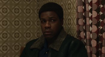Movie still from “Small Axe” (2020), directed by Steve McQueen – A young man in a green jacket is looking at the camera; Close Up shot, Over the shoulder angle