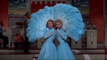 Movie still from “White Christmas” (1954), directed by Michael Curtiz – A pair of women in blue dresses holding large blue feathers; Medium shot, Low angle