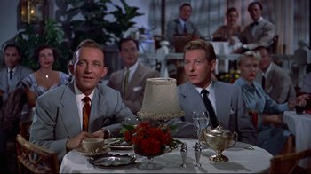 Movie still from “White Christmas” (1954), directed by Michael Curtiz – Two men sitting at a dinner table in suits; Medium shot, Low angle
