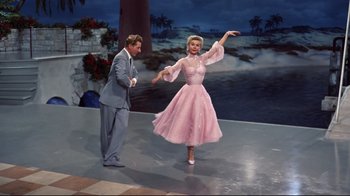 Movie still from “White Christmas” (1954), directed by Michael Curtiz – A man and a woman are dancing on stage in front of palm trees; Wide shot, Low angle