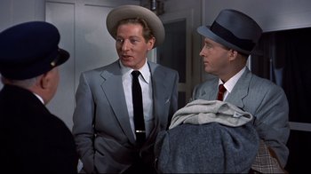 Movie still from “White Christmas” (1954), directed by Michael Curtiz – A man in a suit and a hat standing next to another man in a hat; Medium shot, Over the shoulder angle