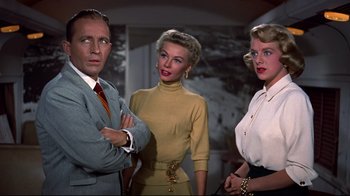 Movie still from “White Christmas” (1954), directed by Michael Curtiz – A man and two women standing next to each other in a room; Medium shot, Low angle