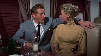 Movie still from “White Christmas” (1954), directed by Michael Curtiz – A man and a woman sitting at a table with a glass of milk in front of them; Medium shot, Over the shoulder angle