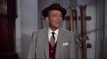 Movie still from “White Christmas” (1954), directed by Michael Curtiz – A man in a suit and hat standing in front of skis; Medium shot, Over the shoulder angle