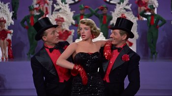 Movie still from “White Christmas” (1954), directed by Michael Curtiz – A group of men standing next to a woman in a black dress; Medium shot, Low angle
