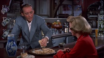 Movie still from “White Christmas” (1954), directed by Michael Curtiz – A man and a woman are serving food to each other; Medium shot, Over the shoulder angle