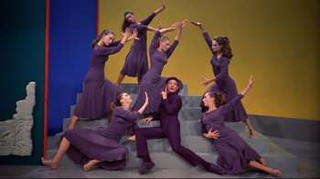 Movie still from “White Christmas” (1954), directed by Michael Curtiz – A group of women in purple dresses posing for a picture; Wide shot, Low angle