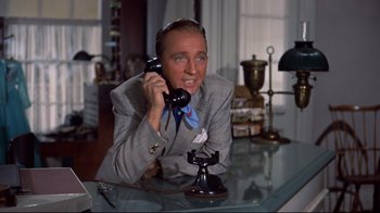 Movie still from “White Christmas” (1954), directed by Michael Curtiz – A man sitting at a table talking on a phone; Medium shot, High angle