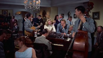 Movie still from “White Christmas” (1954), directed by Michael Curtiz – A group of people sitting at a table with musical instruments; Wide shot, High angle