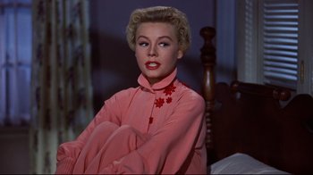 Movie still from “White Christmas” (1954), directed by Michael Curtiz – A woman sitting on top of a bed wearing a pink dress; Medium shot, Low angle
