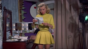 Movie still from “White Christmas” (1954), directed by Michael Curtiz – A woman in a yellow dress looking at a piece of paper; Medium shot, Over the shoulder angle