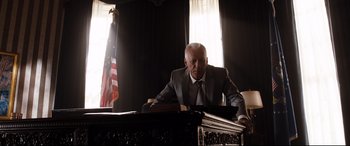 Movie still from “White House Down” (2013), directed by Roland Emmerich – An older man sitting at a desk in a suit and tie; Medium shot, Low angle