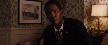 Movie still from “White House Down” (2013), directed by Roland Emmerich – A man wearing a suit and tie sitting in front of a picture; Close Up shot, High angle