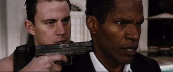 Movie still from “White House Down” (2013), directed by Roland Emmerich – A man holding a gun next to another man in a suit; Close Up shot, Over the shoulder angle