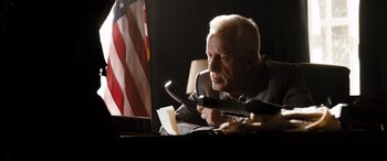 Movie still from “White House Down” (2013), directed by Roland Emmerich – An older man sitting in front of an american flag; Medium shot, Low angle