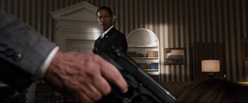 Movie still from “White House Down” (2013), directed by Roland Emmerich – A man in a suit holding a gun in a room; Medium shot, Over the shoulder angle