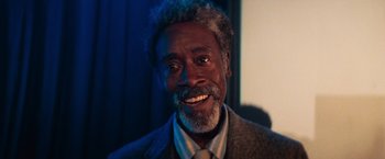 Movie still from “White Noise” (2022), directed by Noah Baumbach – A person wearing a suit and tie smiling; Close Up shot, Low angle