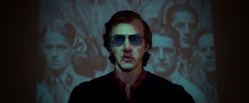 Movie still from “White Noise” (2022), directed by Noah Baumbach – A man wearing sunglasses in front of an image of adolf hitler; Close Up shot, Low angle
