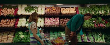 Movie still from “White Noise” (2022), directed by Noah Baumbach – A woman pushing a shopping cart in front of a display of vegetables; Medium shot, Over the shoulder angle
