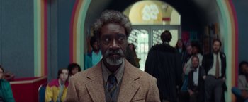 Movie still from “White Noise” (2022), directed by Noah Baumbach – A man with a beard and a suit and tie in front of a crowd of onlookers; Medium shot, Low angle
