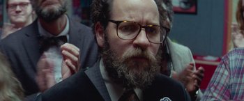 Movie still from “White Noise” (2022), directed by Noah Baumbach – A man with a beard wearing glasses and a suit; Close Up shot, Low angle