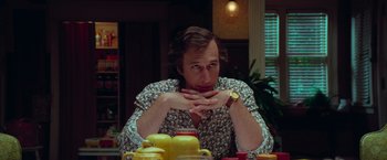 Movie still from “White Noise” (2022), directed by Noah Baumbach – A man sitting in front of a table with a watch; Medium shot, Low angle